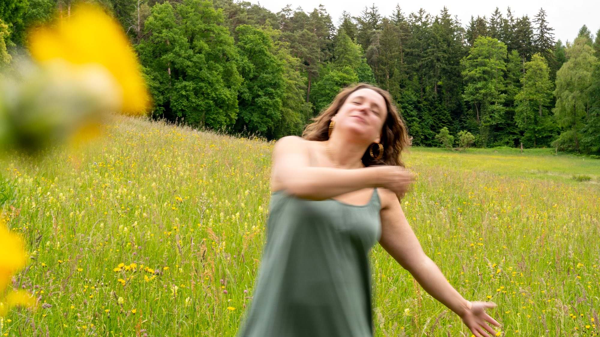 Kaya Zina tanzt in einer Blumenwiese, die Arme in Bewegung